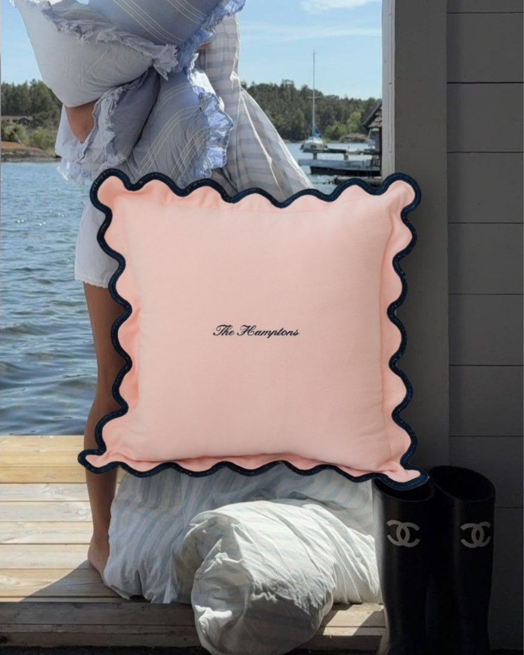 Stylish scalloped throw pillow in soft pink with navy trim, featuring 'The Hamptons' embroidered design.