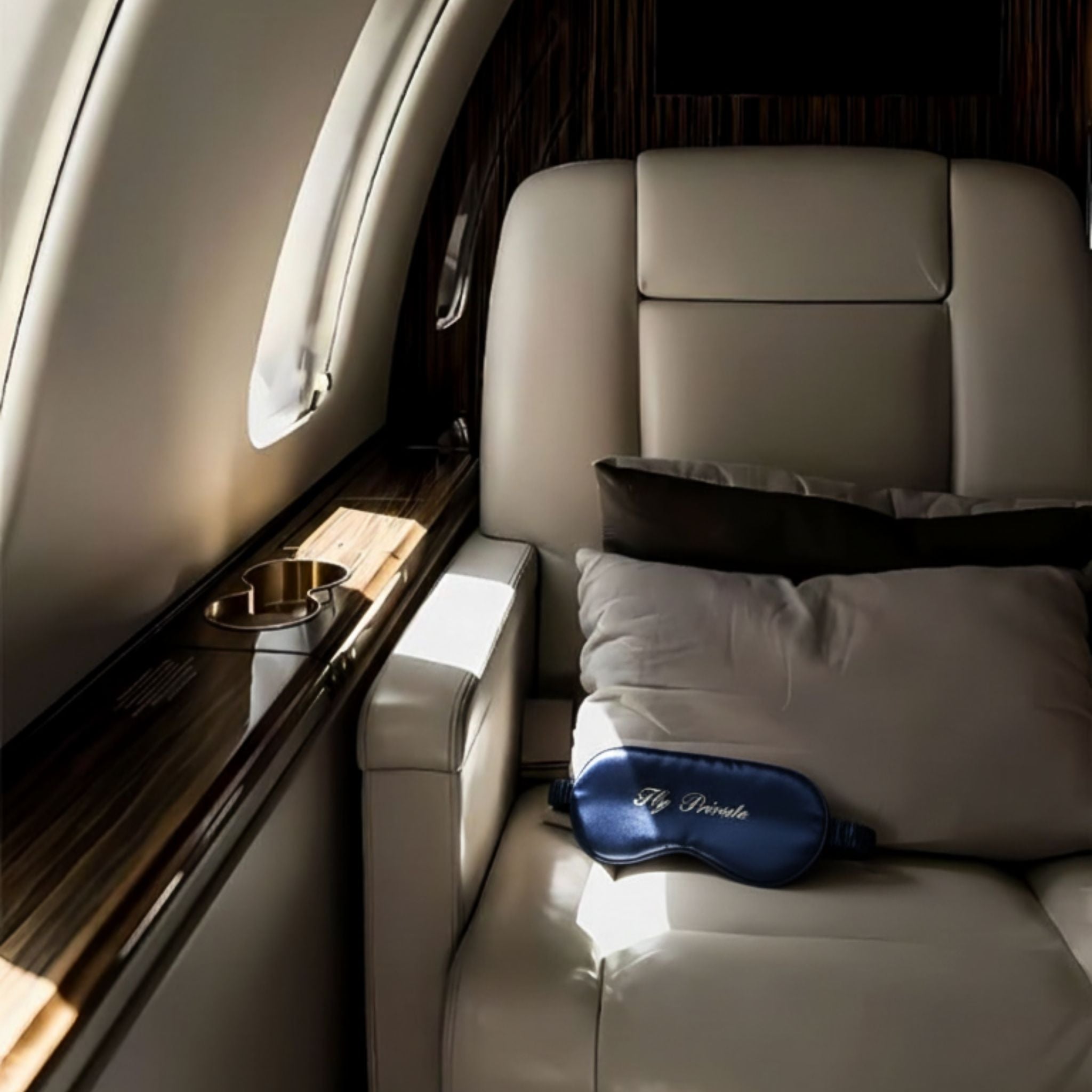 Luxury airplane seat with a soft cream leather finish, accented by a navy silk eye mask and a cozy pillow.