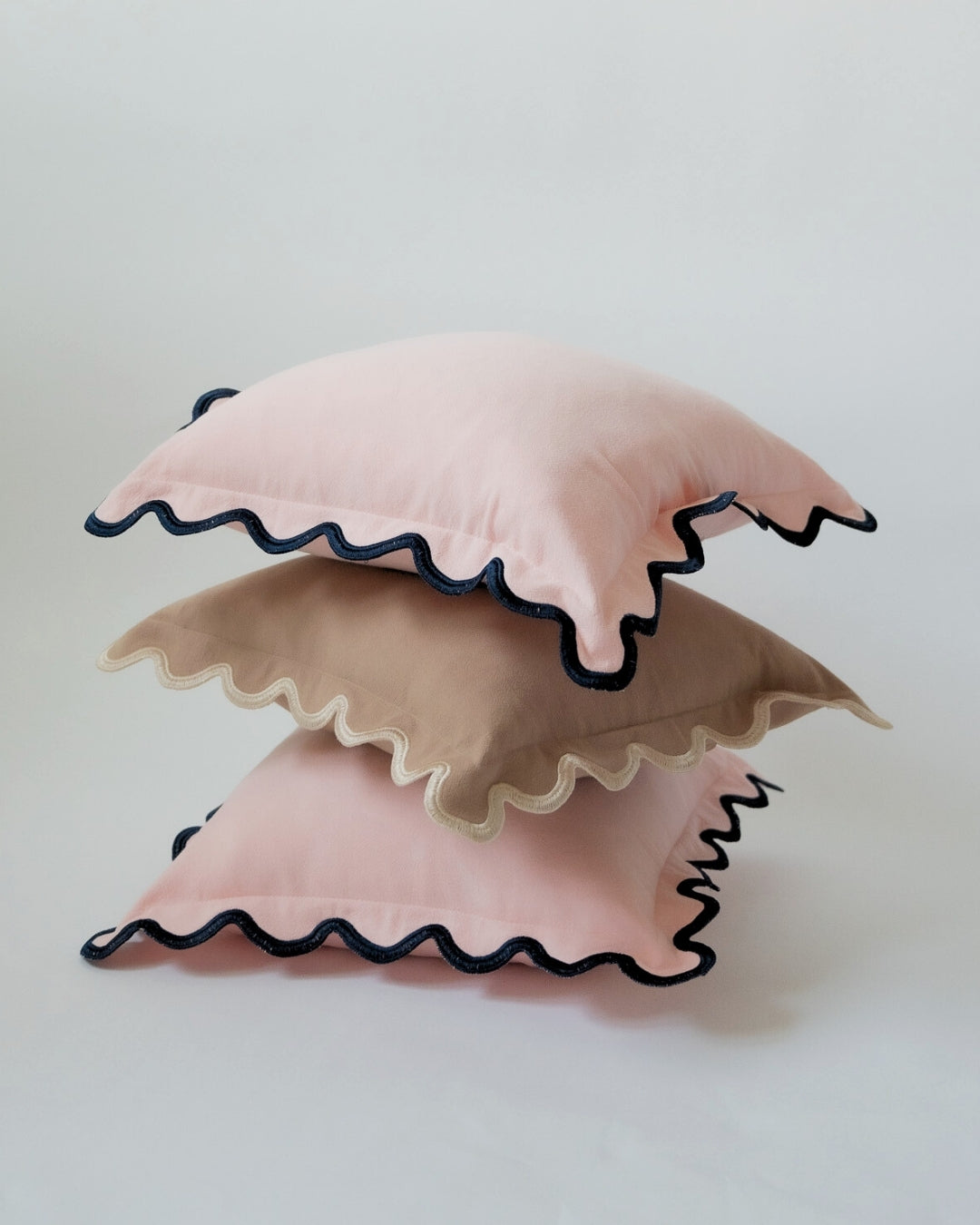 Stack of decorative pillows in pink and beige with scalloped edges and contrasting trim.