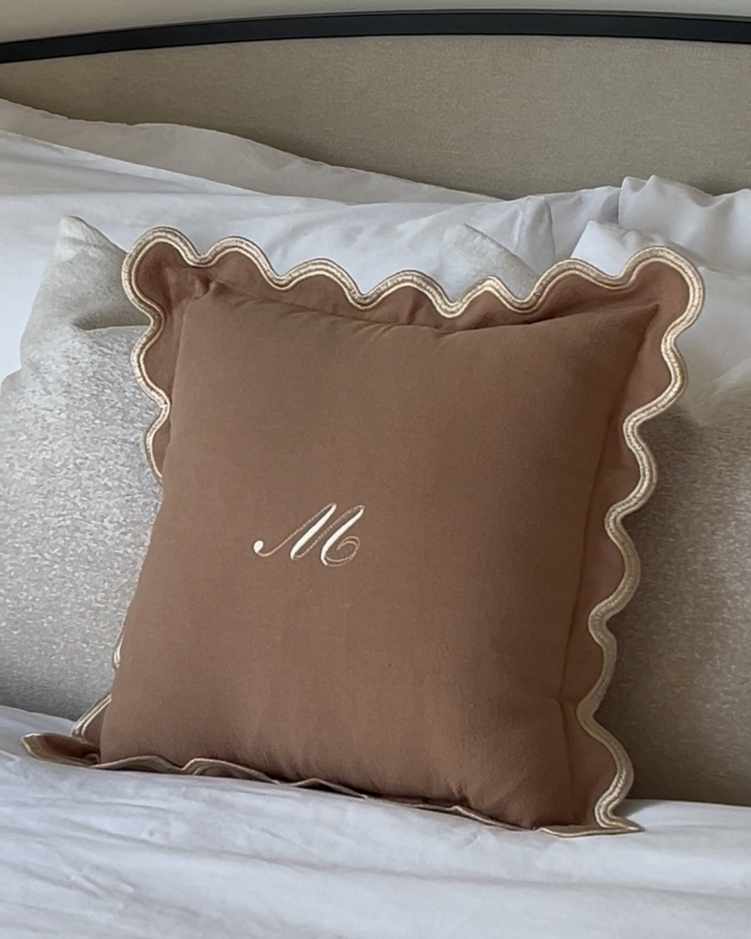 Brown decorative pillow with scalloped edges and embroidered 'M', perfect for cozy home decor.