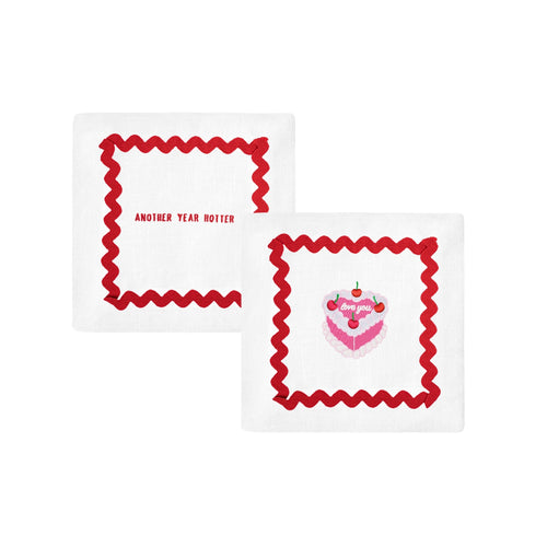 Festive white napkin with red trim and cake design; embroidered with 'love you' and 'another year hotter'.