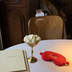 Elegant gold dessert cup filled with whipped cream, red satin sleep mask reading 'Lucky', stylish setting.