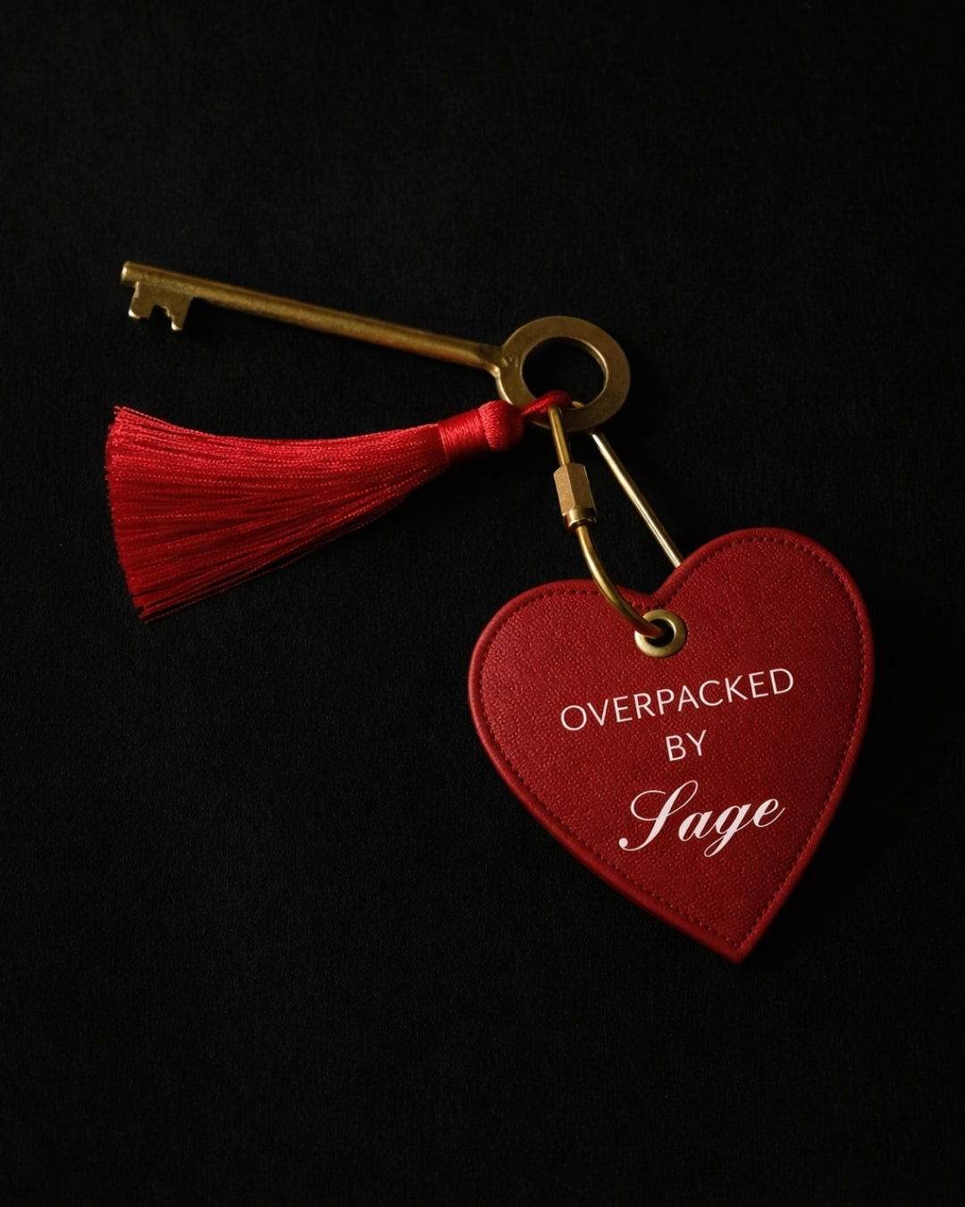 Red heart-shaped keychain with tassel and gold key, featuring 'OVERPACKED BY Sage' in elegant font.