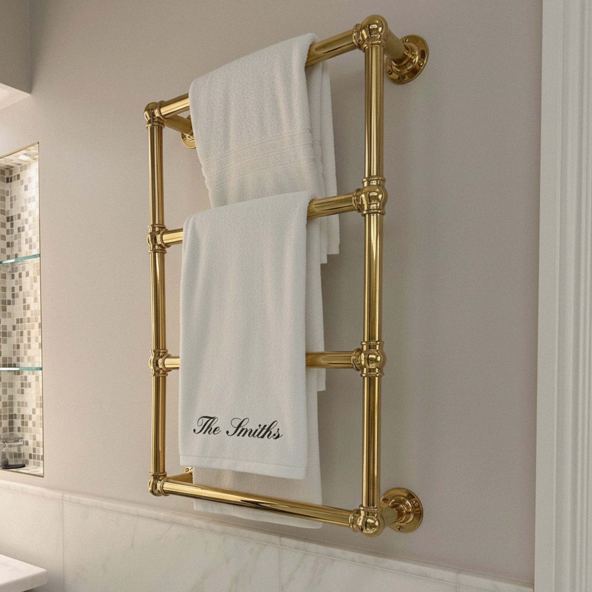 Luxury gold towel rack holding two fluffy white towels, personalized with 'The Smiths'.