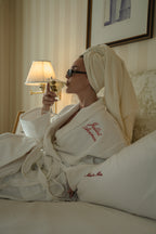 Model in a white, plush bathrobe enjoying a martini, featuring embroidered details in a luxurious setting.