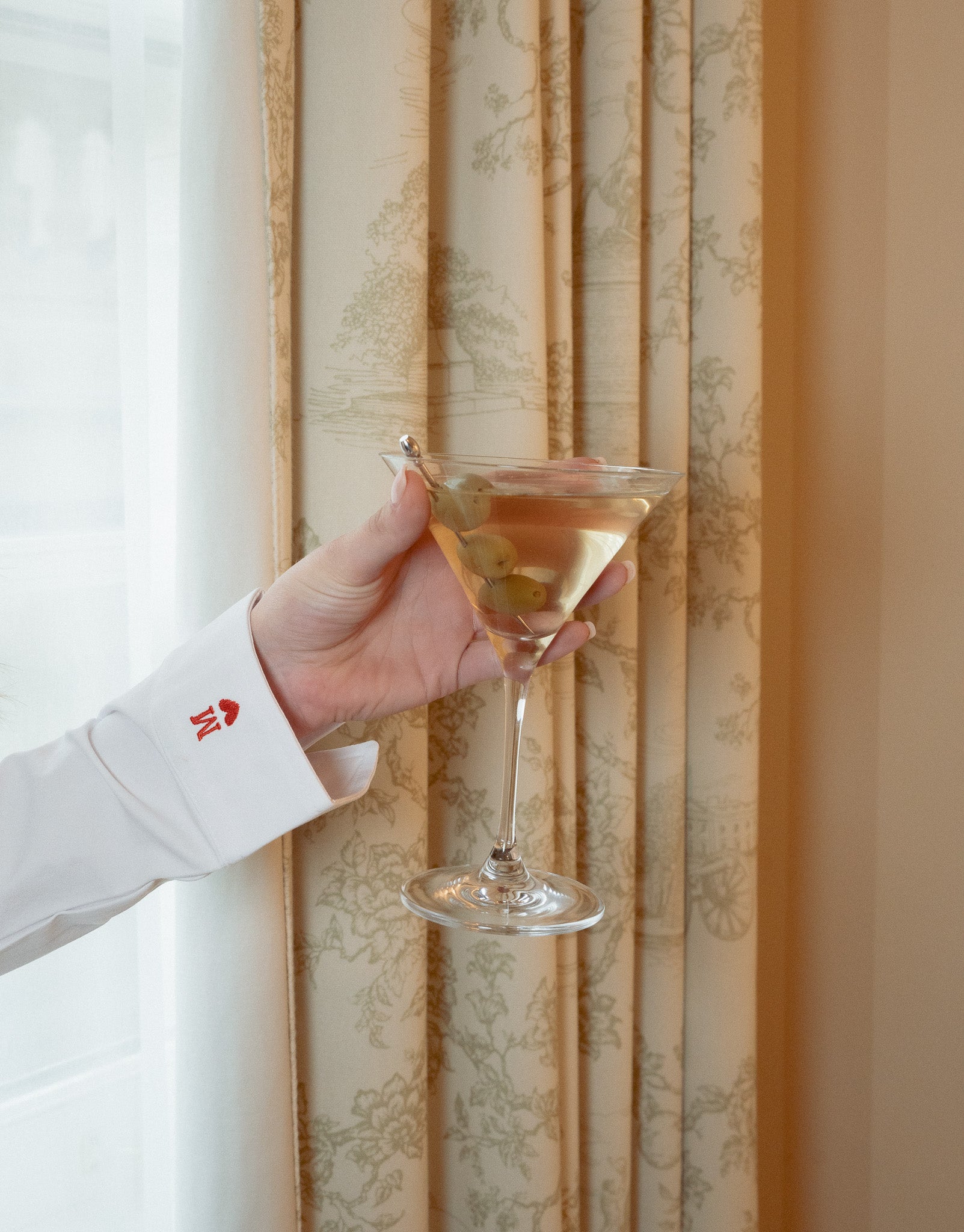 Crisp white dress shirt with red detailing, holding a classic martini with olives in elegant glass.