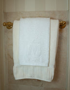Luxurious white cotton towels with embossed 'M' hanging on a gold towel rack.
