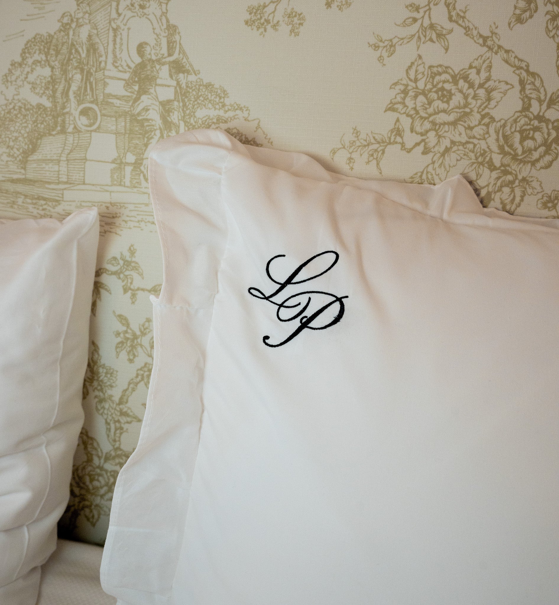 Luxury white pillow with elegant black embroidered initials LP on a stylish patterned background.