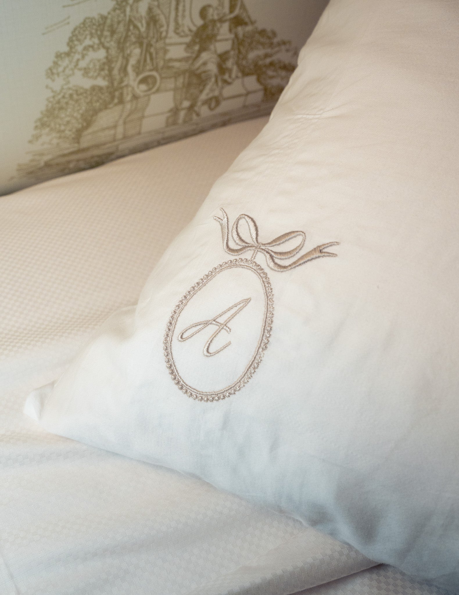 Elegant white pillow with embroidered monogram 'A' and decorative bow detail, perfect for personalized decor.