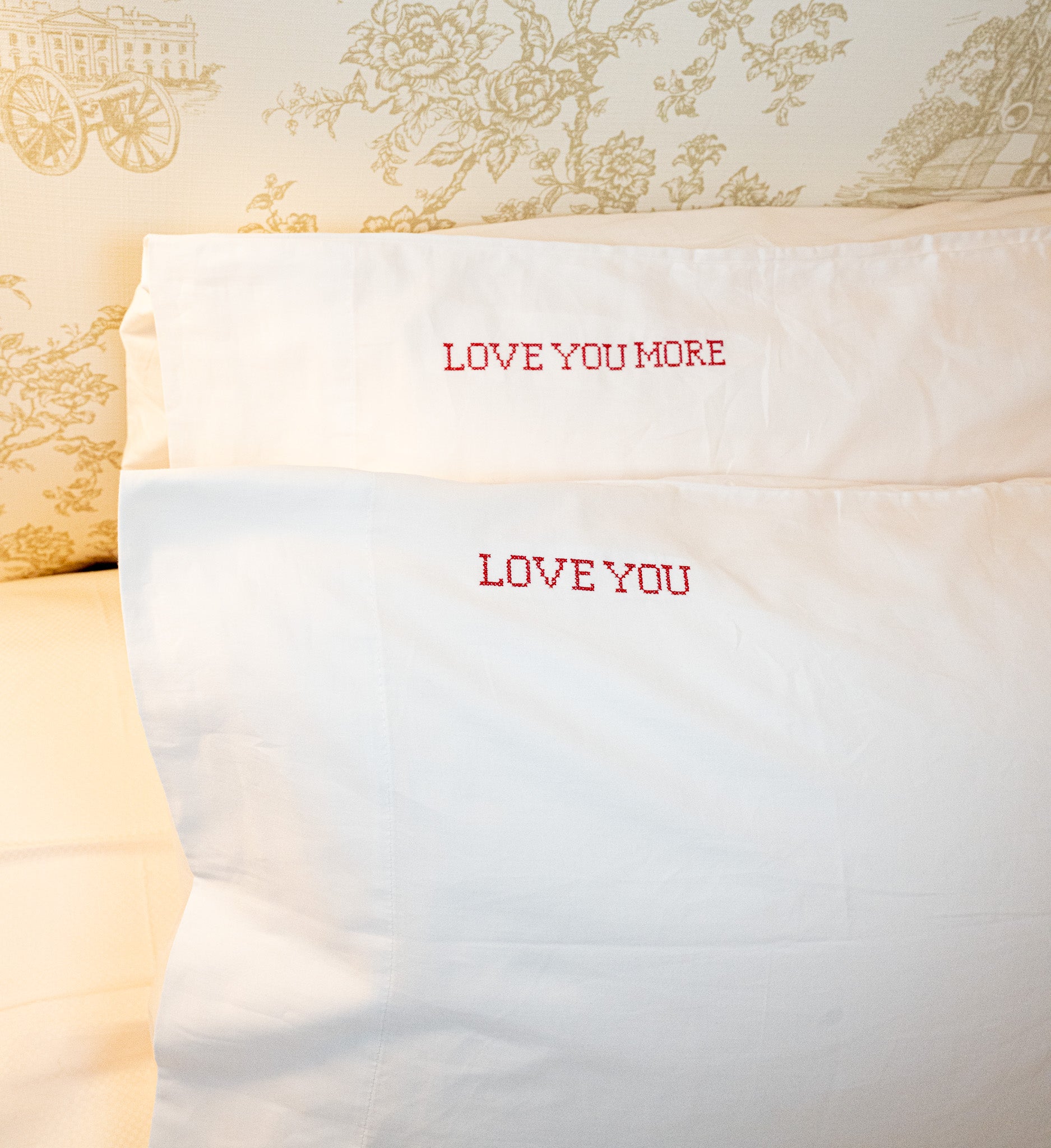 White cotton pillowcases featuring red embroidered phrases 'LOVE YOU' and 'LOVE YOU MORE'.