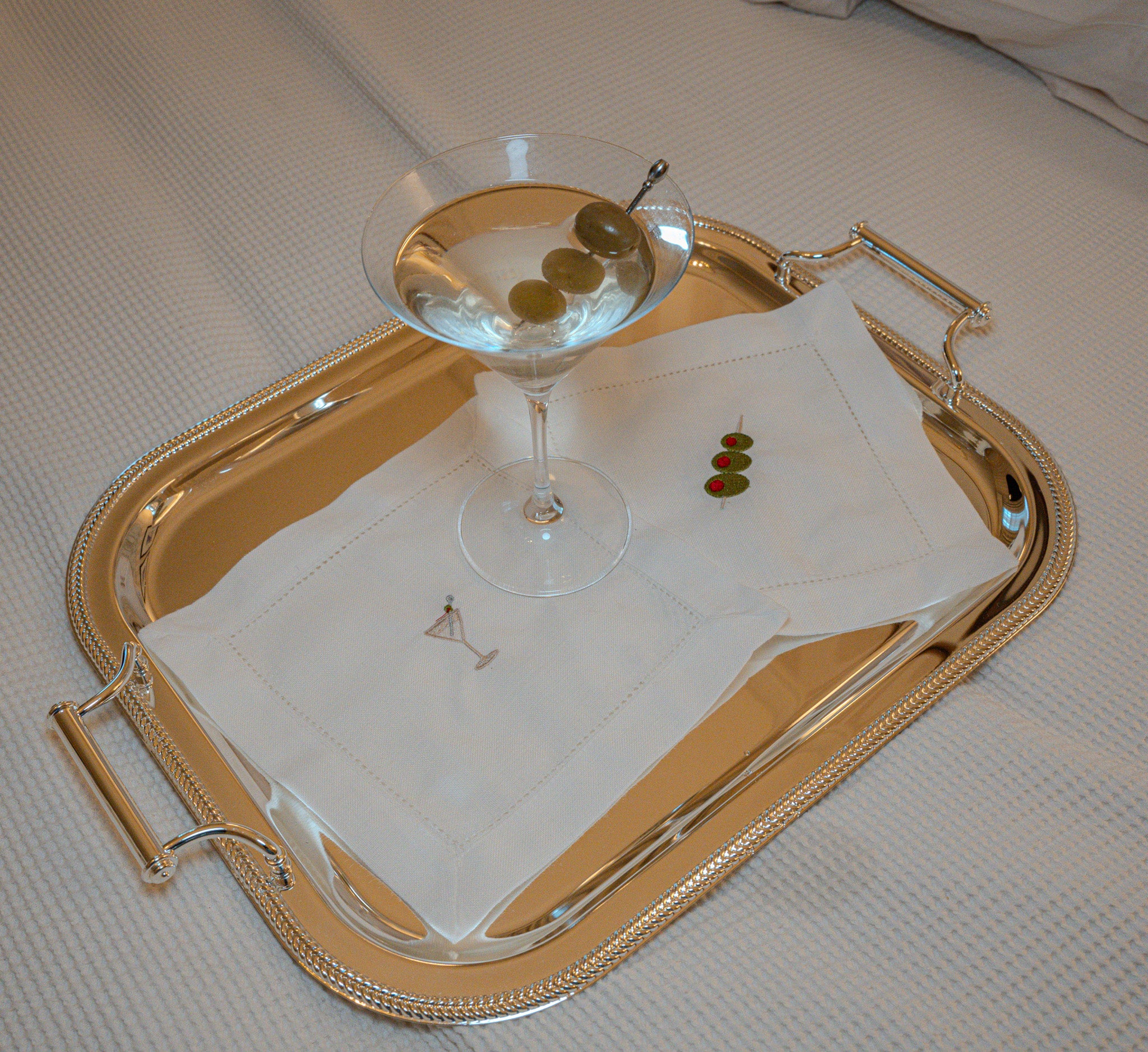 Elegant silver serving tray with a martini glass, olives, and decorative napkins.