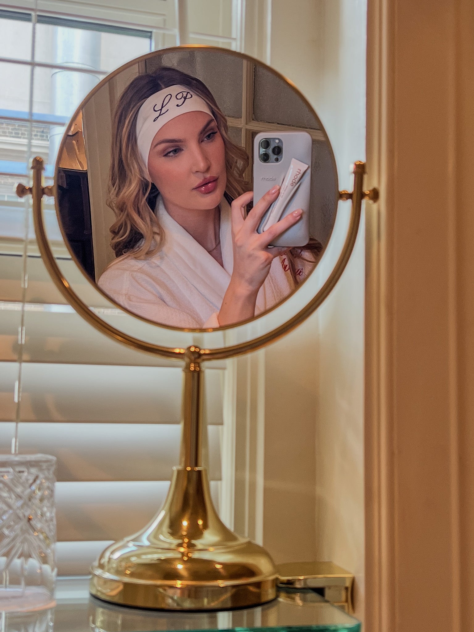 Elegant gold two-sided mirror with a woman wearing a personalized white headband, reflecting beauty routine.