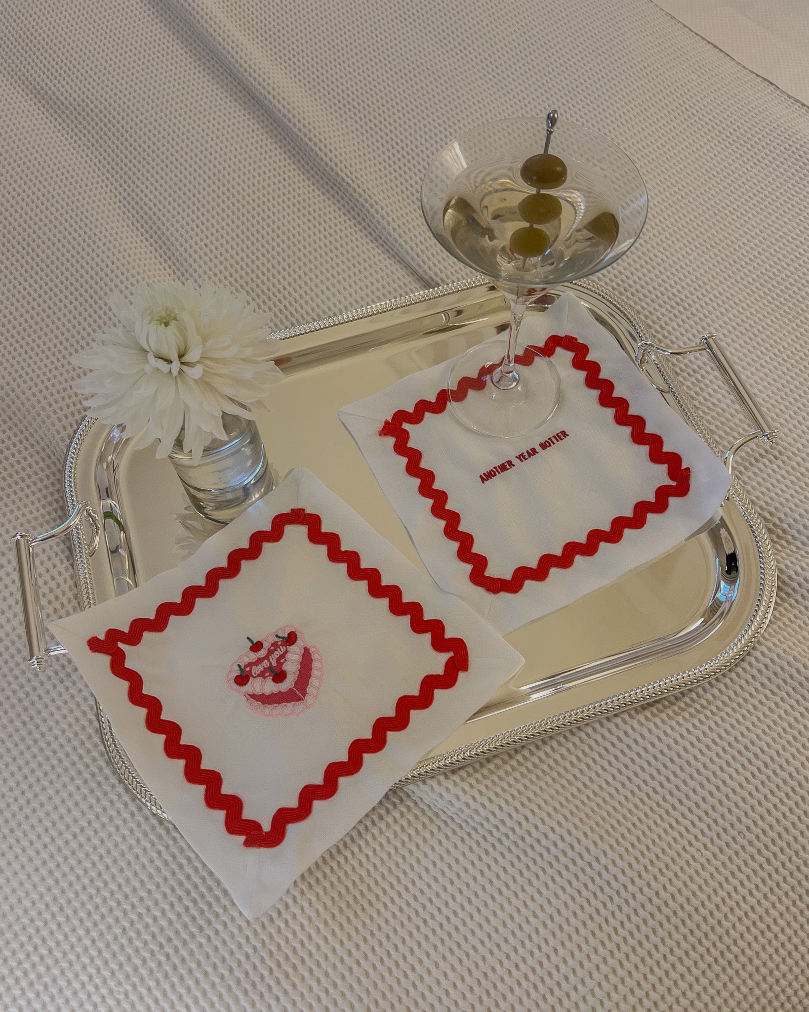 Set of embroidered napkins with red scalloped trim, featuring cake design and text 'Another Team Dinner'.