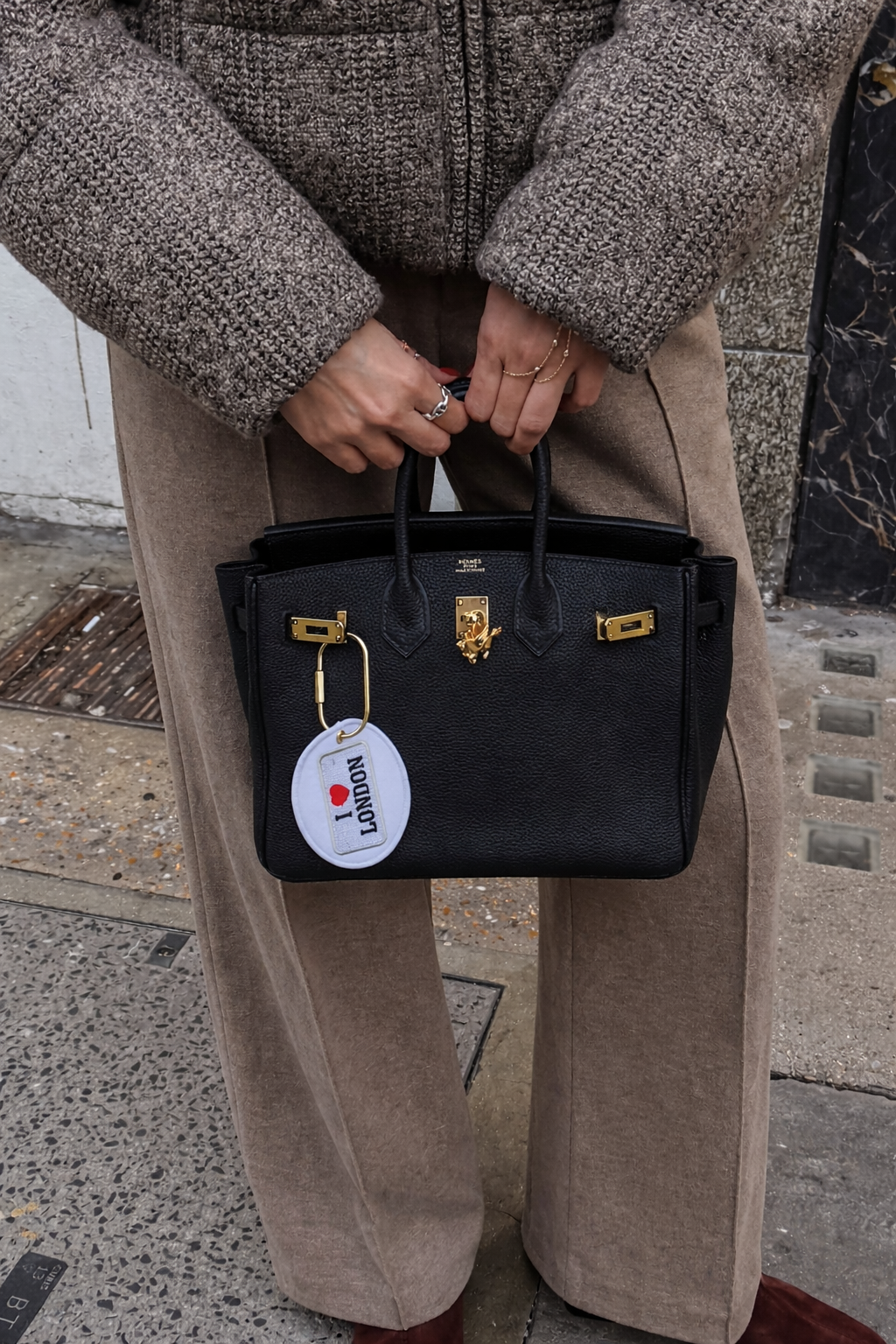 Elegant black leather handbag with gold accents and 'I ❤️ London' tag, worn casually.