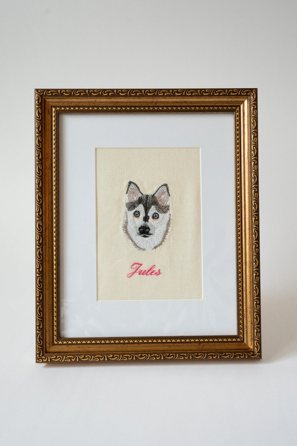 Framed embroidery of a husky dog with name 'Jules', on beige fabric with a gold ornate frame.