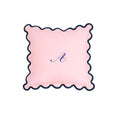 Pink decorative pillow with scalloped edges and embroidered monogram 'A.' in navy blue.