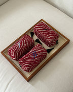Three rolled red and white zebra-print knit items, likely socks or small accessories, arranged in a wooden tray on a light fabric surface.