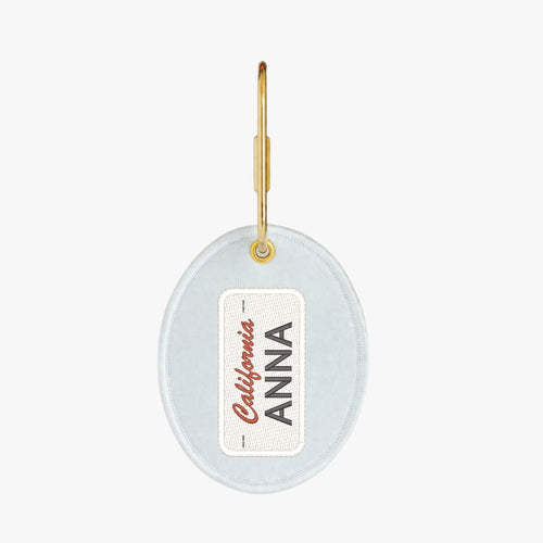 Personalized oval keychain in light blue with gold hardware and customizable name tag.