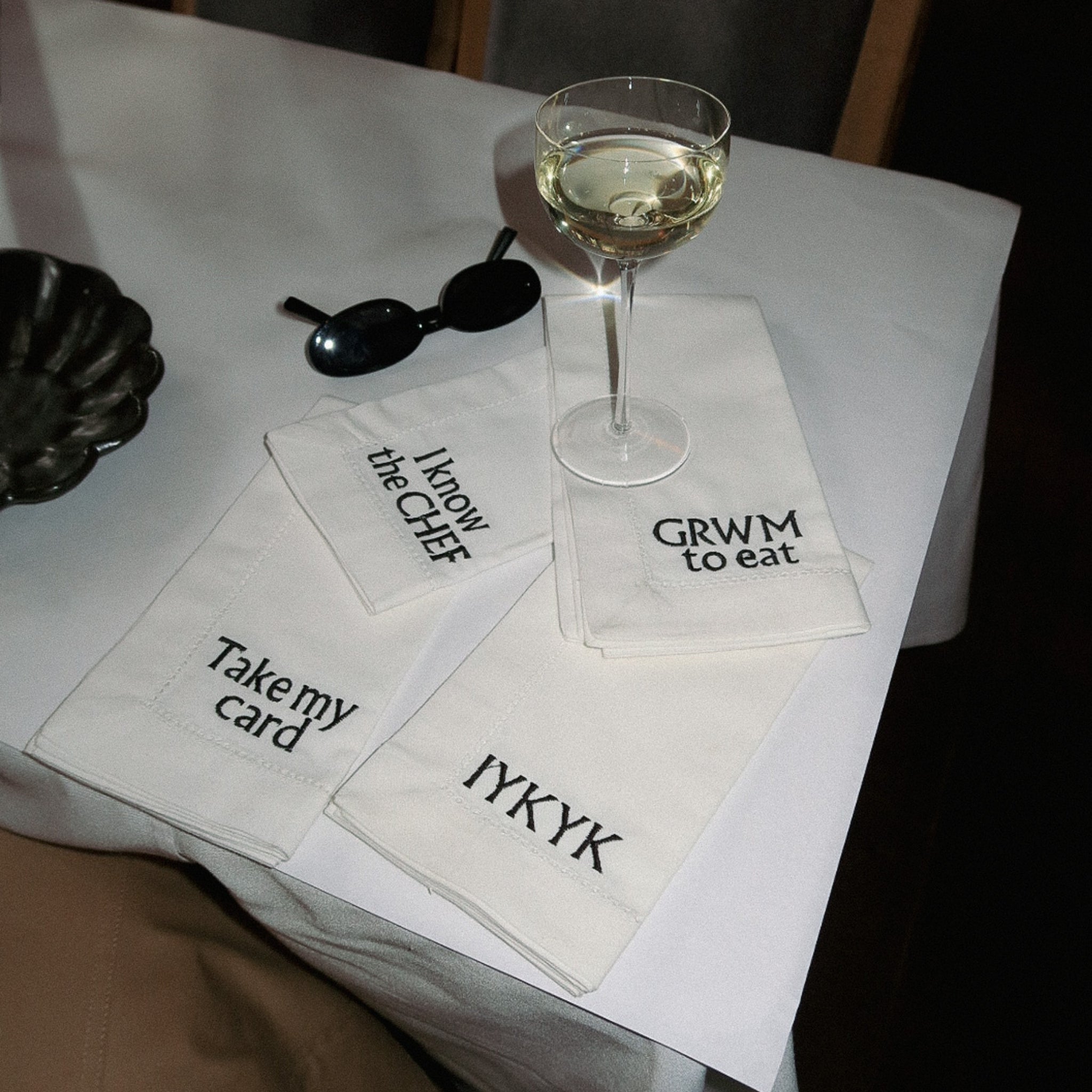 Set of four white embroidered napkins with trendy phrases, perfect for stylish dining decor.