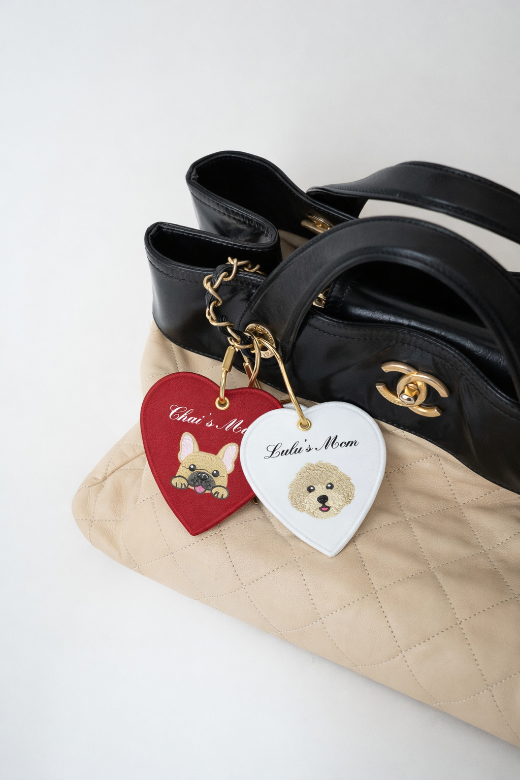 Black leather handbag with quilted beige base, featuring embroidered pet-themed heart keychains.