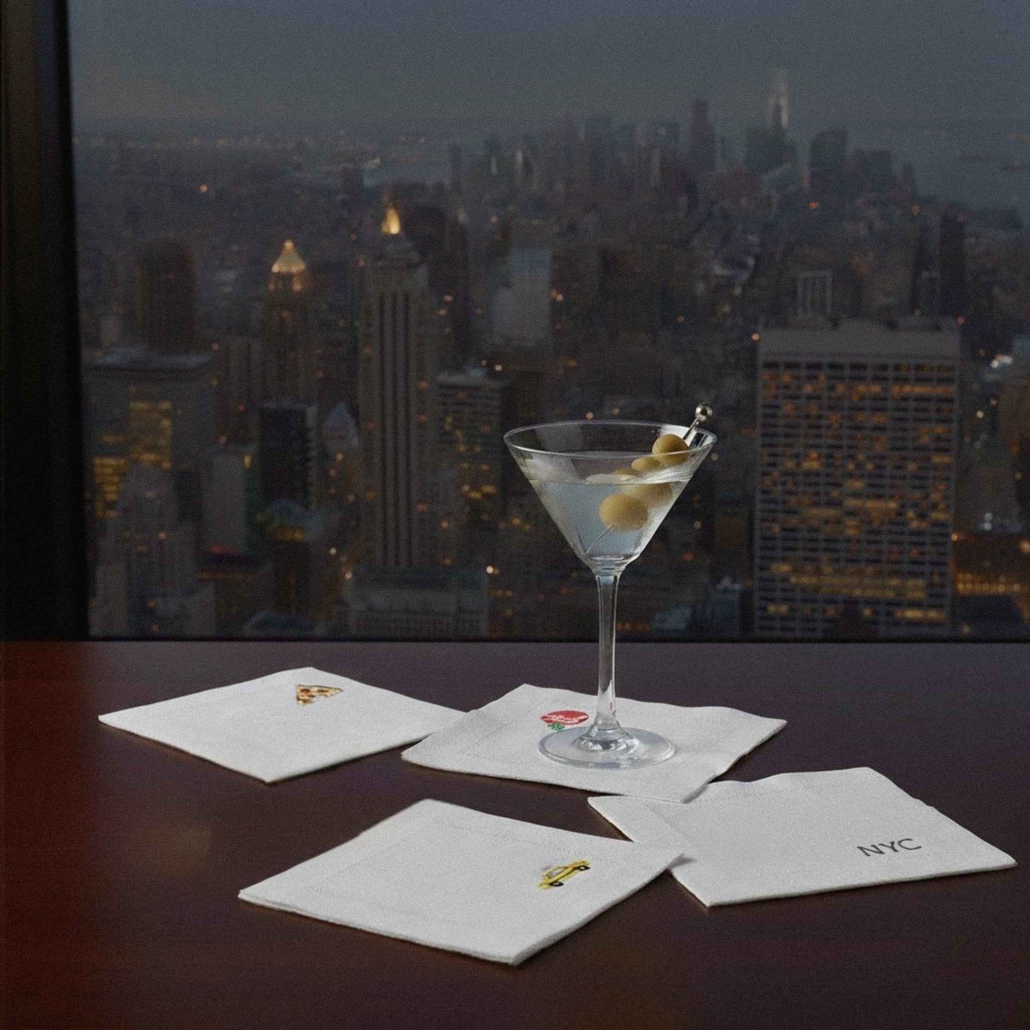 Elegant white cocktail napkins with NYC design, featuring fun icons and a martini in a stylish bar setting.