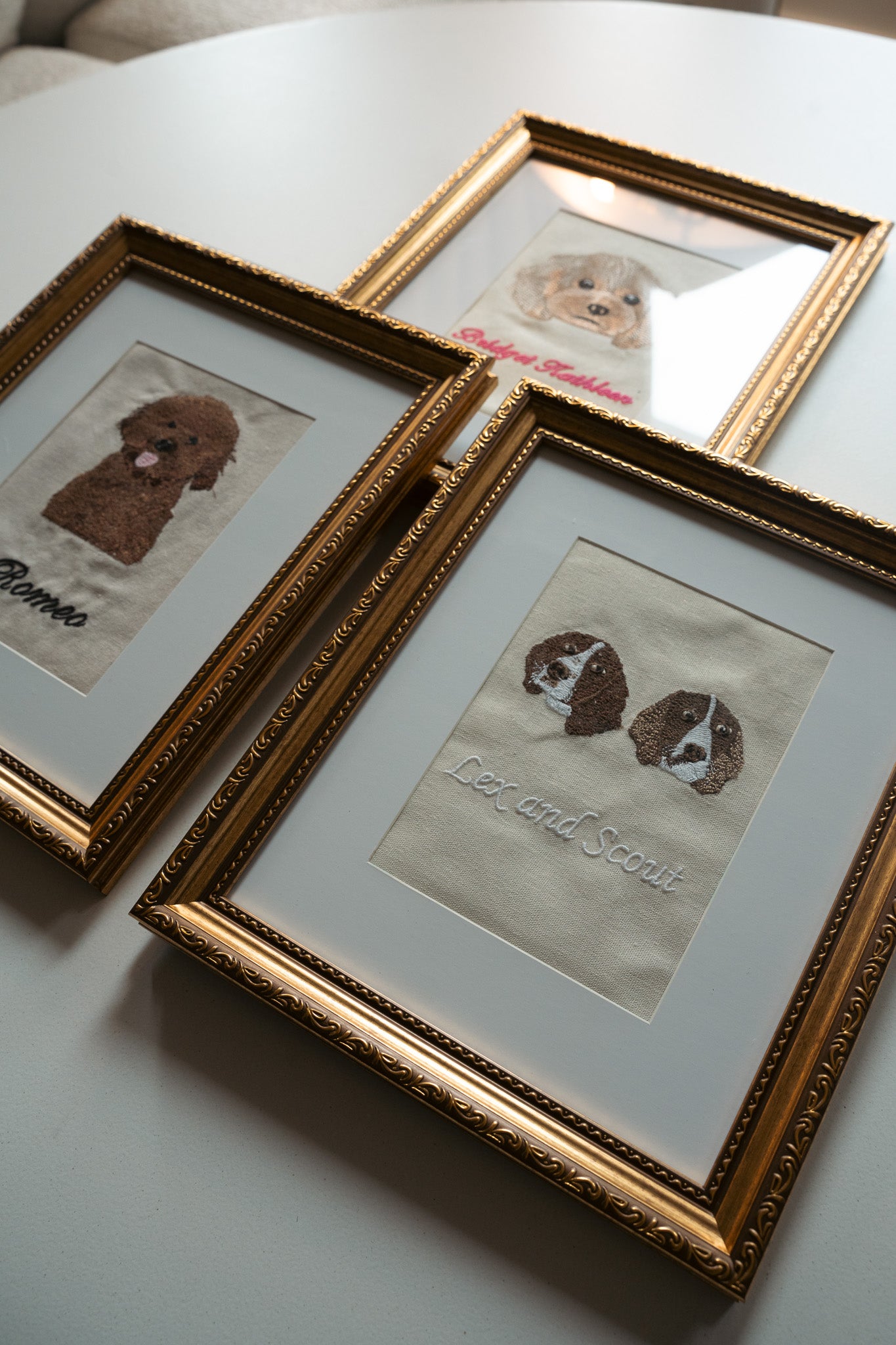 Three framed embroidered pet portraits featuring a brown dog and two spaniels, gold ornate frames.