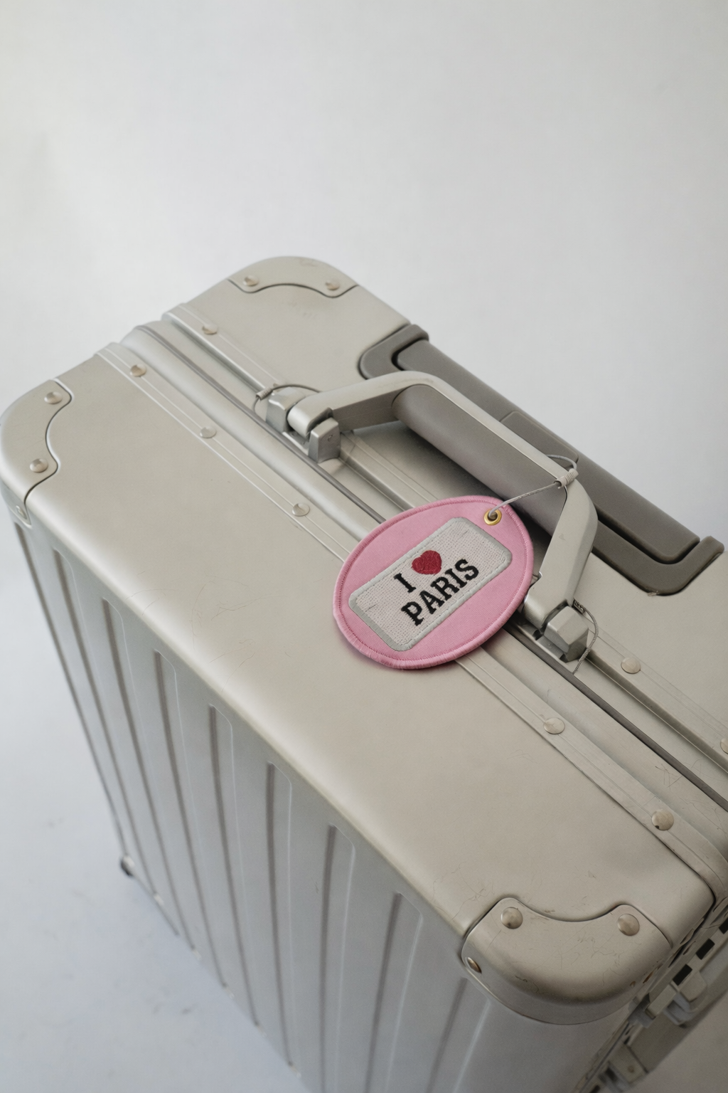 Silver suitcase with a pink 'I Love Paris' luggage tag attached, perfect for stylish travel.