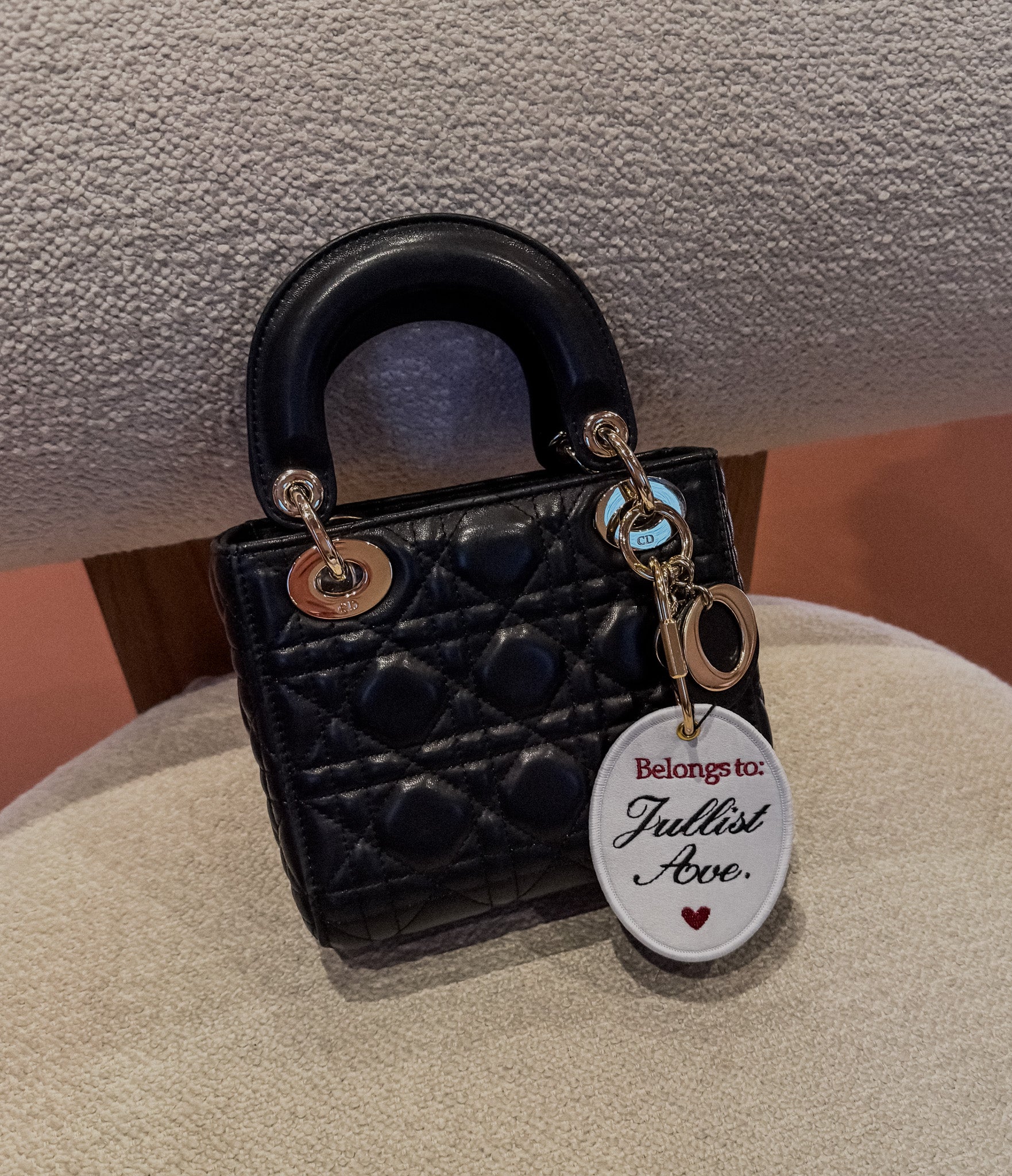 Small black quilted handbag with charm, 'Belongs to: Jullist Avo.' Elegant leather design.
