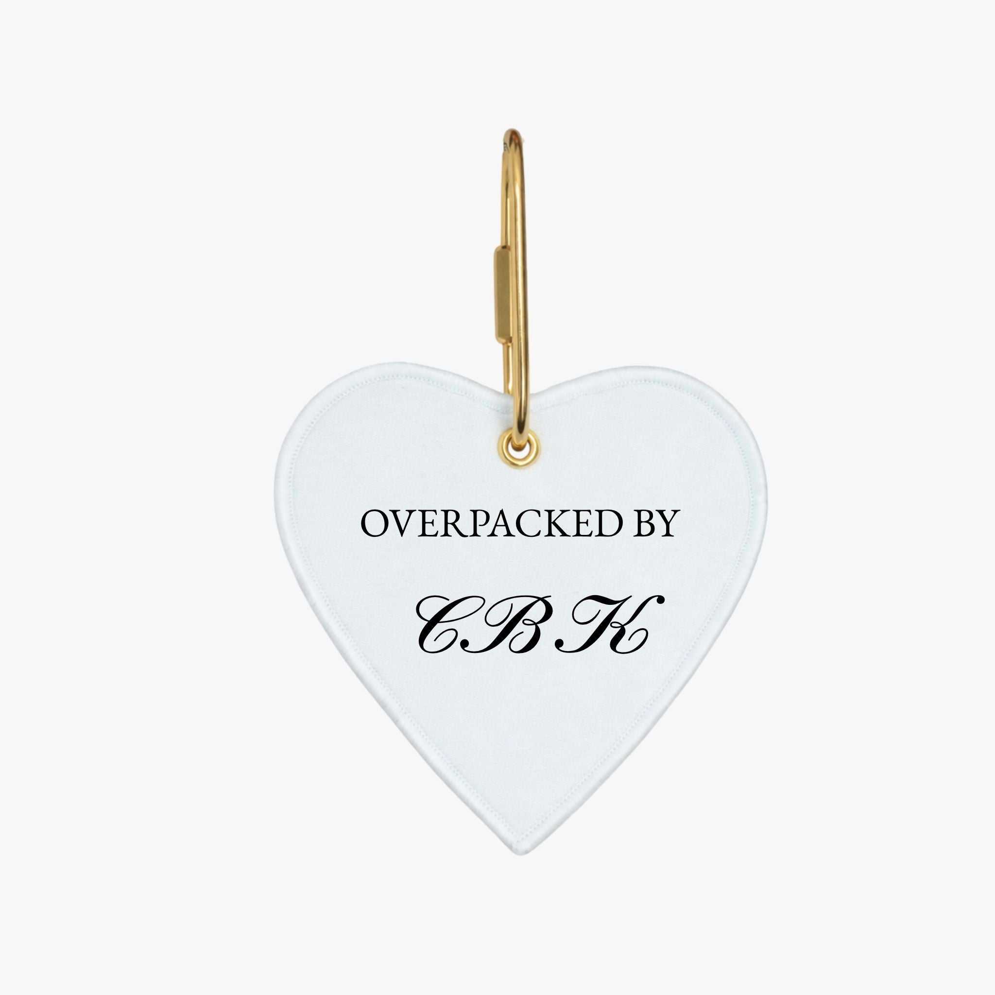 Heart-shaped luggage tag in white with 'OVERPACKED BY CBK' in elegant black script.