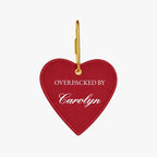 Red heart-shaped luggage tag with gold hook, personalized with 'Overpacked by Carolyn'.