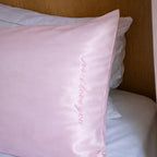 Pink satin pillow with embroidered text on a bed