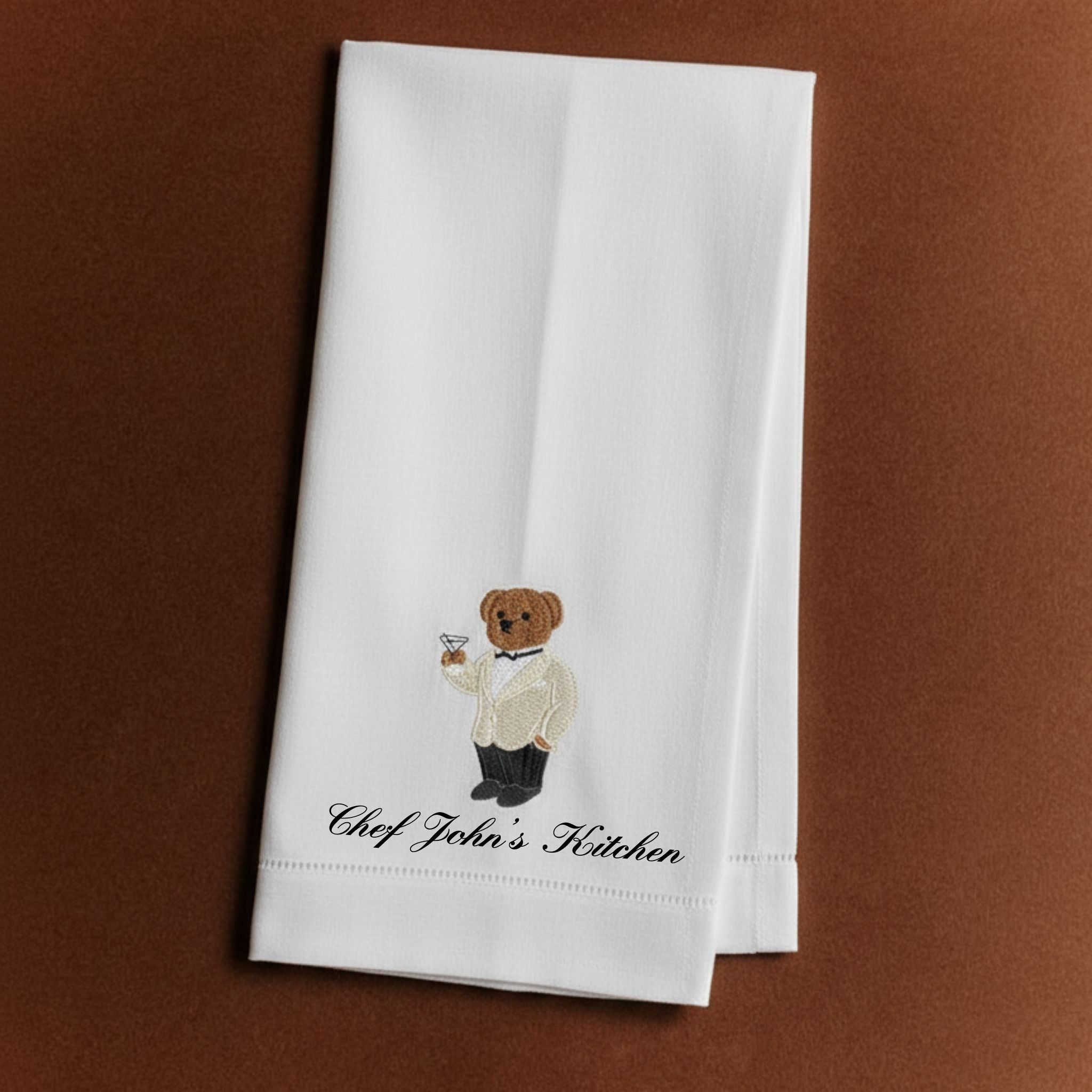 White kitchen towel with embroidered bear chef and 'Chef John's Kitchen' text, perfect for stylish cooking.