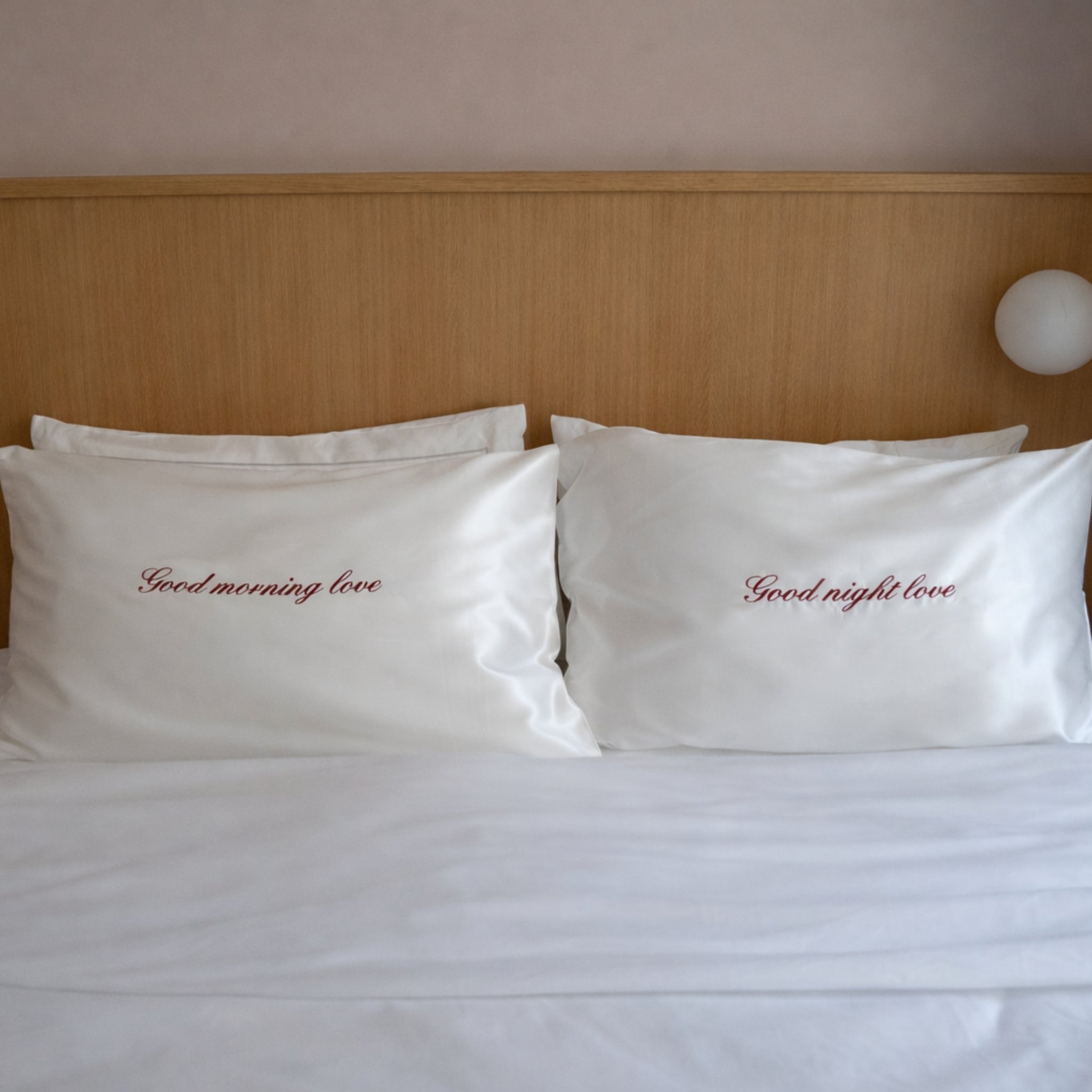 Two white pillows with embroidered text on a bed with a wooden headboard.