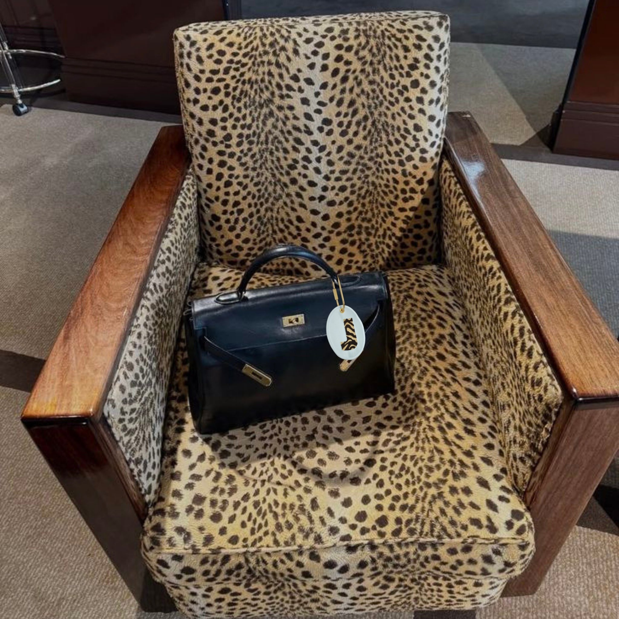 Stylish black leather handbag on leopard print armchair, featuring elegant gold accents.